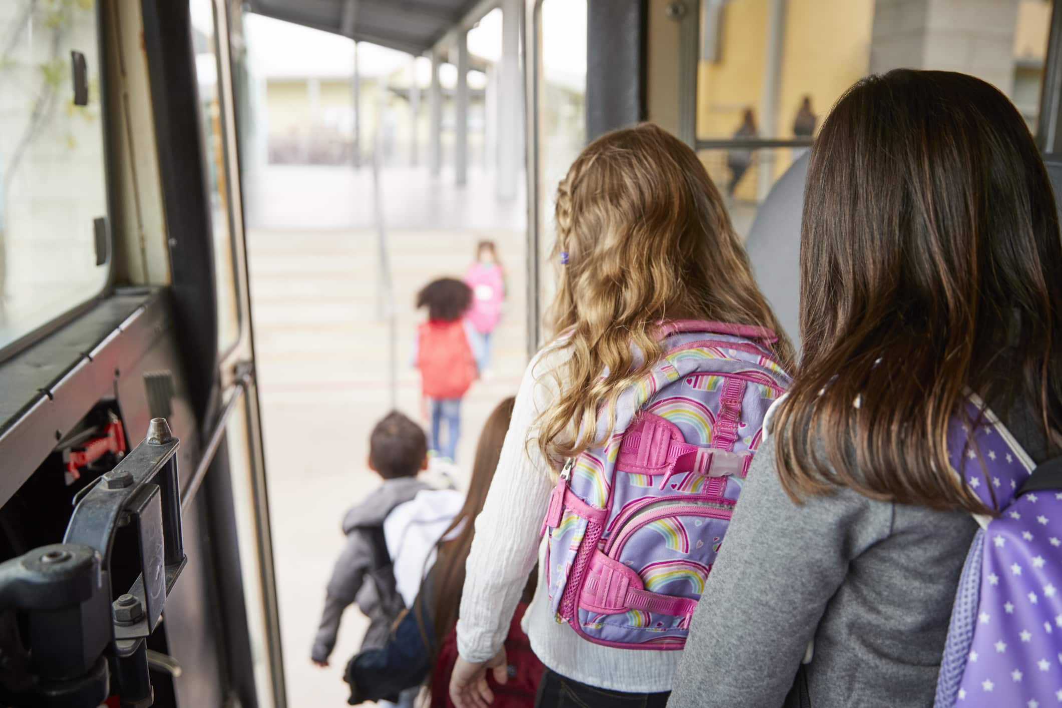 Two girls waiting behind their friends to get off school bus
